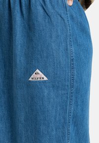 Denimrok in lichtblauw met een gathered tailleband. Beschikt over een Quiksilver logo patch in een witte driehoekige vorm aan de zijkant.