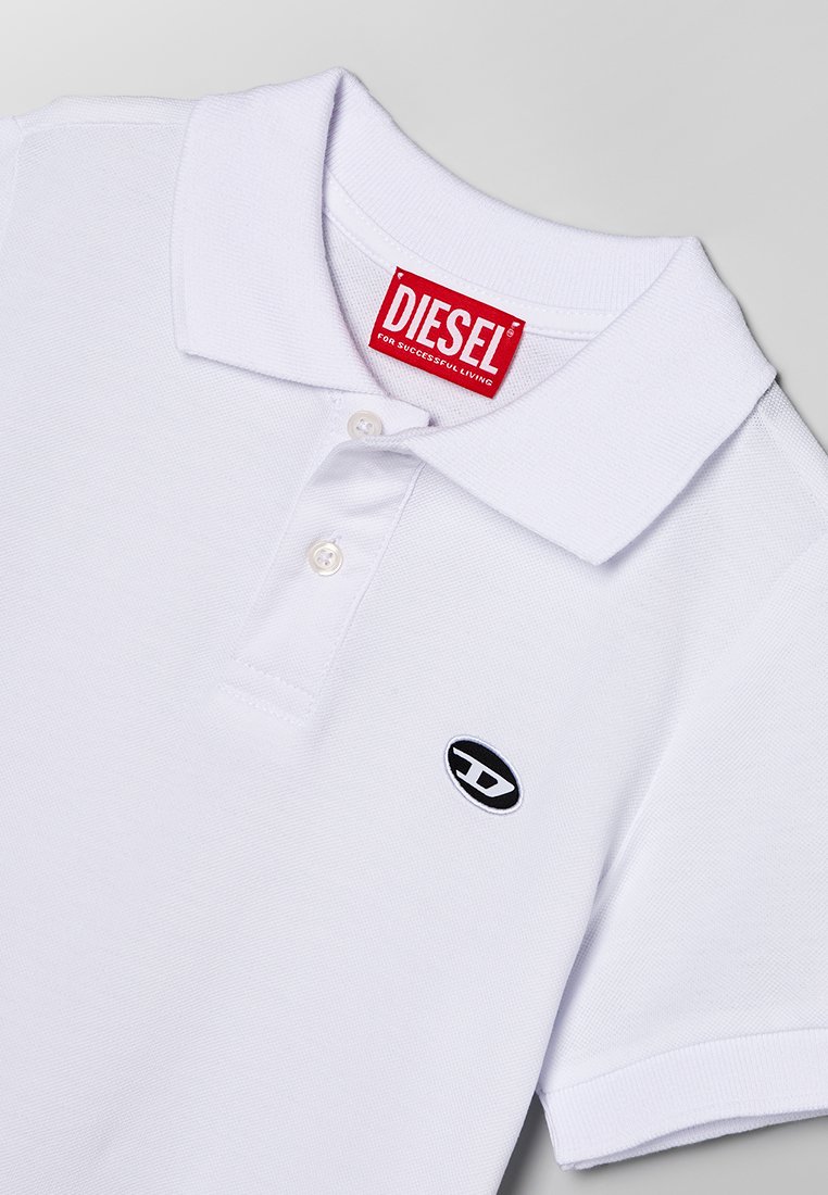 Polo bianco in cotone, caratterizzato da un'etichetta rossa Diesel, una patta con tre bottoni e un piccolo logo ovale nero sul petto.