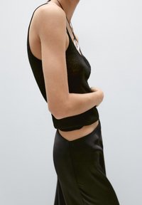 Black ribbed tank top with thin straps, fitted design, paired with sleek black satin pants. Simple and minimalist aesthetic.