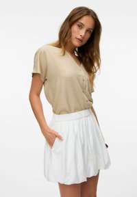 Beige blouse met korte mouwen en een V-hals, met knoopdetails, gecombineerd met een witte rok met een verzamelde elastische taille en zijzakken.