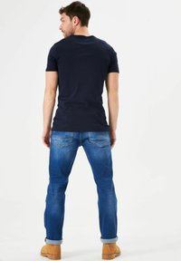 Camiseta de manga corta de color azul marino combinada con unos vaqueros de mezclilla de color azul claro. Los vaqueros tienen bolsillos traseros con costuras sutiles y los puños doblados.