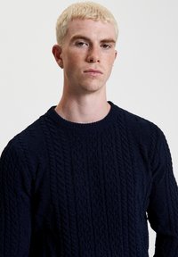 Maglione blu navy a maglia cable con colletto rotondo, motivo testurizzato e maniche lunghe. Realizzato in un materiale spesso e lavorato a maglia.