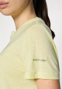 Light yellow short-sleeve t-shirt made of soft material, featuring a subtle logo embroidered on the sleeve. Smooth texture, relaxed fit.