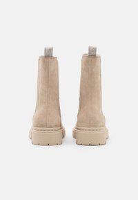 Bežové semišové kotníkové boty s robustní gumovou podrážkou, které mají kontrastní podpatek a smyčkové poutka vzadu pro snadné obouvání.