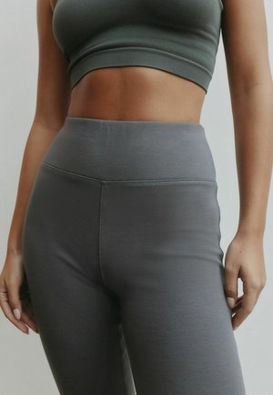 Colanți gri, talie înaltă, realizați dintr-un material neted și elastic, cu un design fără cusături și cusături subtile, asortați cu un top scurt asortat.