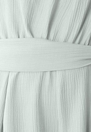 Svetlo zelena teksturirana obleka iz tkanine s gubami in širokim, usklajenim pasom okoli pasu, ki ima zgubano površinsko vzorčenje.