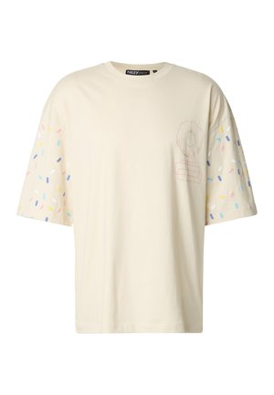 Krém színű rövid ujjú póló, színes szórócukor mintákkal az ujjain, és egy fánk grafikával az elején. Könnyű pamut anyagból.
