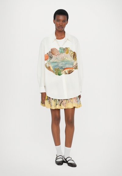 White long-sleeve shirt with colorful shell and landscape print at the center, paired with a pleated yellow skirt featuring floral patterns.