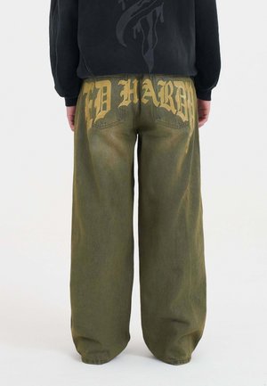 Pantalones de pierna ancha en verde olivo hechos de denim, con un gran texto amarillo en la parte trasera con un efecto desvanecido. Bolsillos traseros visibles.