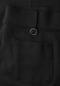 Close-up van zwarte stoffen broek met een achterzak en een kleine zilveren ring bevestigd bij de tailleband.