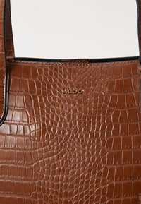 Bruine nep-krokodillenleren totebag met dunne hengsels en een gouden ALDO-logo gecentreerd aan de voorkant.