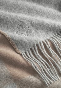 Grau gefühlte Decke mit fransigen Rändern, die ein dezentes besticktes Blütenmotiv und eine weiche Textur aufweist. Unterer Rand in einem beigen Farbton.