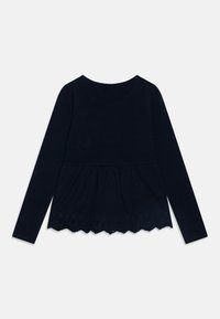 Marinblus med lång ärm i peplumdesign, med en scalloped nederdel utsmyckad med intrikata perforerade blommönster. Slät textur.