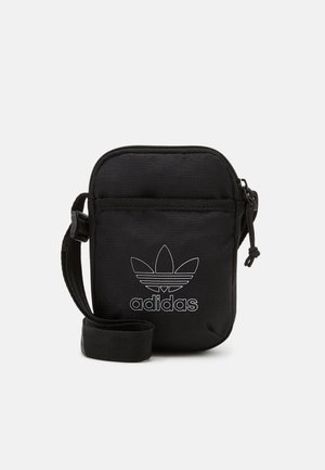 Pochette en tissu noir avec une fermeture éclair, présentant un logo Adidas blanc bien visible et un motif à trois bandes sur le devant. Comprend une sangle amovible.