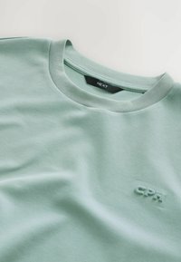 Mintgrøn bomulds T-shirt med rund hals og et hævet "CPH" logo på forsiden. Glat tekstur og let stræk i stoffet.