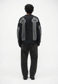 Suéter de punto negro con patrón de columnas blancas en la parte posterior, que presenta una textura esponjosa. Combinado con pantalones oscuros de corte holgado.