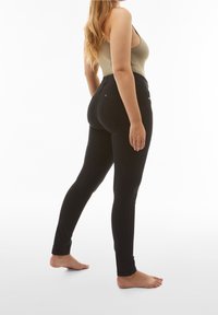 Pantalones vaqueros negros ajustados con una textura suave y un diseño de talle alto. Cuentan con bolsillos traseros y una silueta ajustada. Modelo de pie descalzo.