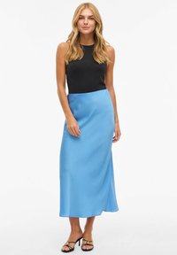 Svart ermeløs topp kombinert med et langt, lyseblått skjørt i sateng. Skjørtet har en subtil glans og en rett silhuett med sidesplitter.