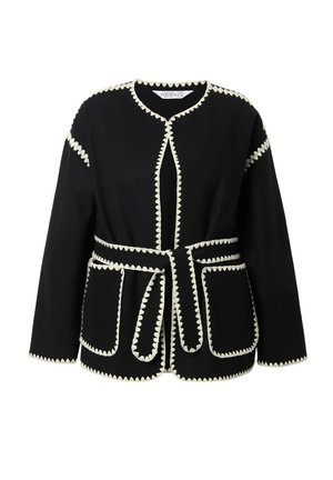 Zwarte langemouwenjas met witte scalloped rand, voorzakken en een bijpassende riem die om de taille is geknoopt.