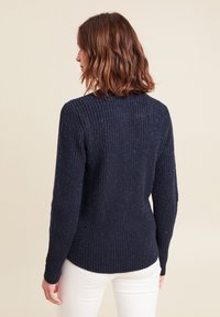 Marineblauer Strickpullover mit gerippter Textur, verziert mit metallischen Fäden und langen Ärmeln, die an der Hüfte enden. Keine sichtbaren Verschlüsse.