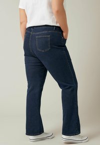 Jeans in denim blu scuro con vestibilità a gamba dritta, dotati di tasche posteriori e vita a media altezza, abbinati a sneakers bianche.