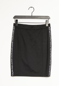 Gonna nera con un design aderente, caratterizzata da un marchio bianco lungo il lato. Realizzata in un materiale liscio e elastico. Appesa a una gruccia nera.
