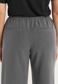 Grijze elastische taillebroek met een gladde textuur, voorzien van twee achterzakken en een relaxte pasvorm, zichtbaar vanuit de achteraanzicht.