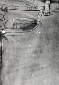 Jeans de mezclilla gris con un bolsillo frontal, sutiles clavos brillantes dispersos por la tela y costuras en contraste.