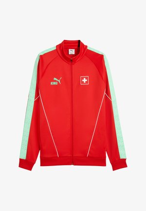 Chaqueta roja de Puma con cremallera, con franjas verde claro en las mangas, detalles de ribete blanco, parche de la bandera suiza y texto "KING" con el logo de Puma en el pecho.