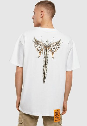 Hvid bomulds T-shirt med et detaljeret, intrikat grafik af stiliserede vinger og pigge på ryggen. Inkluderer et orange mærke på siden.