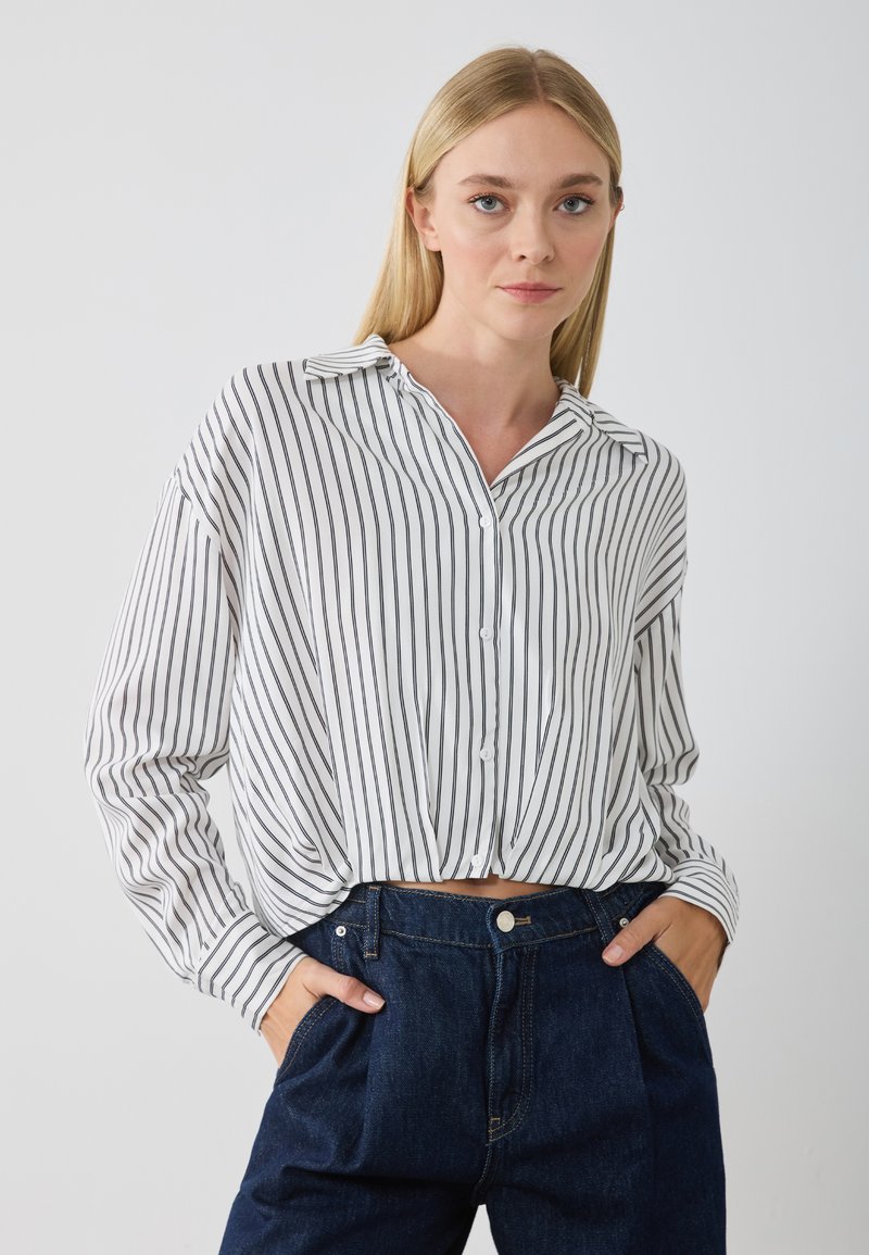 Wit overhemden met zwarte verticale strepen, voorzien van een kraag, lange mouwen en een relaxed fit, gecombineerd met hoog waisted donkere denim jeans.