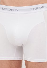 Boxer-culottes en coton blanc avec une ceinture grise arborant "LES DEUX" en lettres majuscules. Tissu lisse avec une coupe ajustée et des coutures plates.
