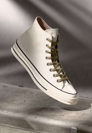 Baskets montantes en toile blanc cassé avec des lacets vert olive, bout renforcé, bande d'accent noir et doublure à carreaux.