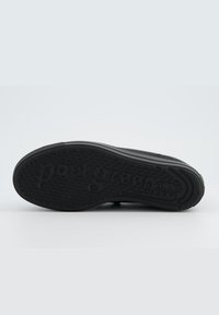 Schwarze Schuhsohle mit kreisförmigem Grip-Muster und eingeprägtem Markennamen. Glatte Textur mit einem dezenten erhöhten Rand und rundem Absatz.