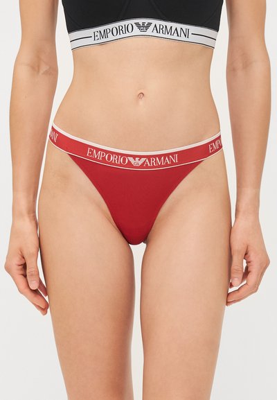 Red thong underwear with a white band featuring "Emporio Armani" logo. Soft fabric, minimalistic design, and a low-rise cut.