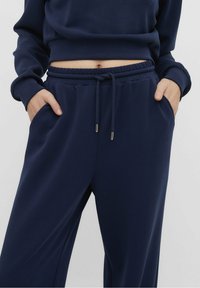Marineblauwe sweatpants met een elastische tailleband, trekkoordsluiting en zijzakken; gladde, zachte textuur zonder zichtbare patronen.