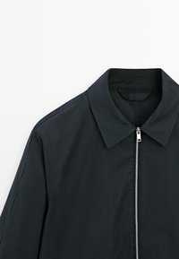 Sort zip-up jakke med krave, der har en glat overflade og diskrete stikninger langs skuldrene.