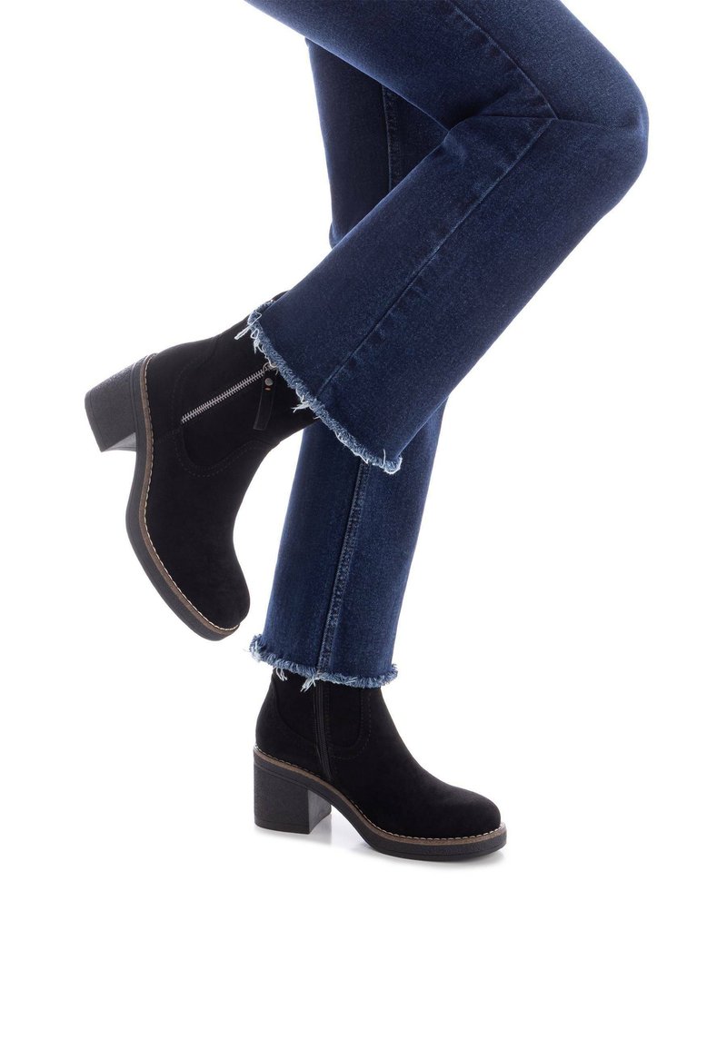 Stivaletti neri in suede con tacco quadrato, zip laterale e dettagli di cucitura a contrasto. Indossati con jeans in denim scuro con orlo sfrangiato.