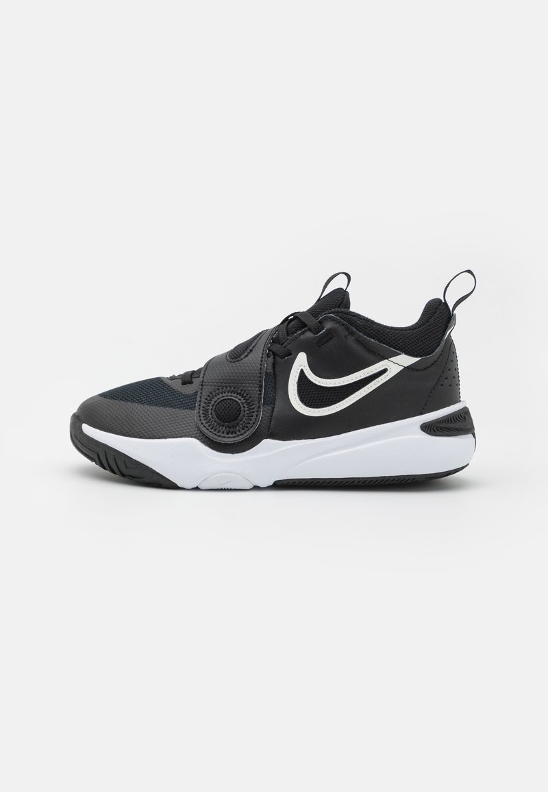 Chaussure de sport noire avec une tige en textile, des accents blancs, un détail de logo circulaire, des superpositions texturées et une semelle en caoutchouc blanche.