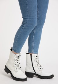 Hvide læder ankelstøvler med blomsterapplikationer og sorte detaljer, med lynlås i siden og struktureret gummisål, parret med blå jeans.