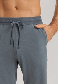 Pánské šedé sportovní kalhoty s hladkým povrchem, elastickým pasem, stahovací šňůrkou a bočními kapsami.