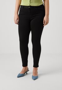 Black skinny jeans with a smooth texture, featuring front pockets and a button closure, paired with blue pointed-toe heels.