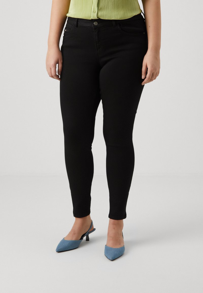 Black skinny jeans with a smooth texture, featuring front pockets and a button closure, paired with blue pointed-toe heels.