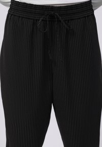 Pantalons à rayures noires avec une taille élastique et un cordon de serrage ajustable. Présente de fines rayures blanches pour un aspect texturé.