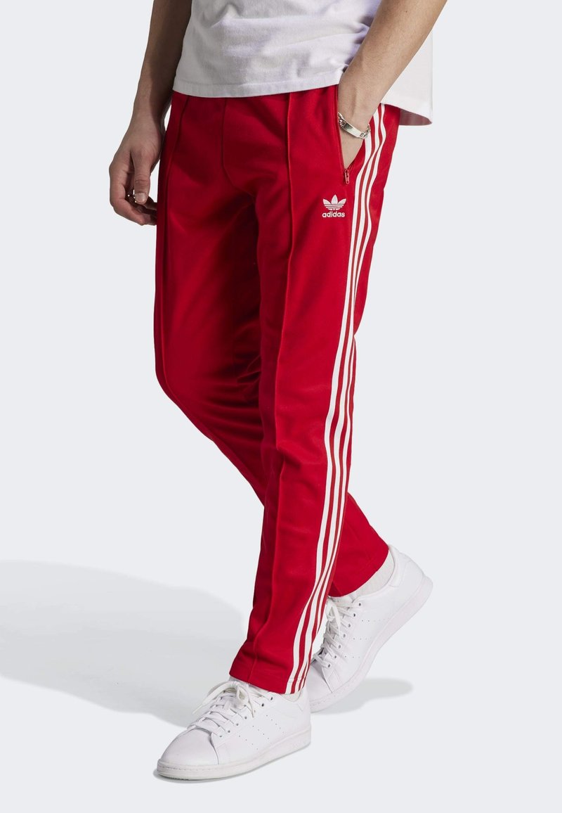 Punaiset urheiluhousut, joissa on valkoinen Adidas-logo ja kolme valkoista raitaa sivuilla. Slim fit -mallinen, valmistettu pehmeästä, tekstuuripinnasta.