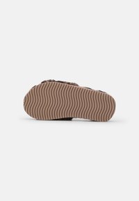 Brown fur slipper with a textured, wavy rubber sole. The fur has a soft appearance; the sole is thick with a pronounced grip pattern.