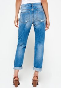 Svetle modré jeansy z denimu s volným střihem, obsahující ohrnuté nohavice a dvě zadní kapsy s jemnými švy.