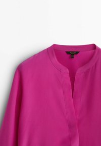 Chemise fuchsia avec un col mandarin, en tissu lisse et léger avec une légère brillance. Le design comprend une ouverture à l'avant et une coupe décontractée.