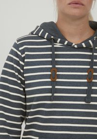 Sudadera a rayas en azul marino y blanco, con capucha ajustable y detalles de hardware en marrón. Tejido suave con un corte relajado.