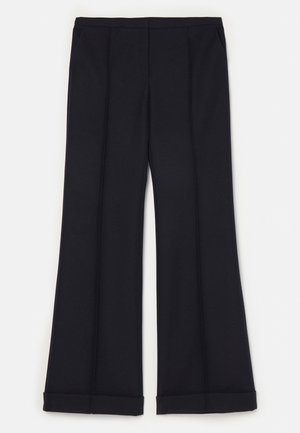 Czarna satynowa bluzka na halter z marszczonym detalem przy szyi, zestawiona z granatowymi dopasowanymi spodniami i wzorzystymi niebieskimi szpilkami.